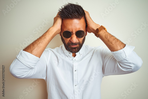Handsome indian buinessman wearing shirt and sunglasses over isolated white background suffering from headache desperate and stressed because pain and migraine. Hands on head.