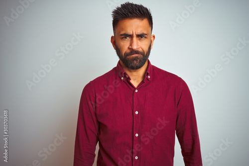 Young indian man wearing red elegant shirt standing over isolated grey background skeptic and nervous, frowning upset because of problem. Negative person.