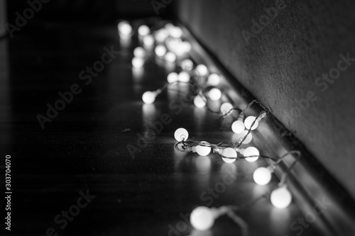 Black and white mood and tone of close up view of decorative wire led small warm white light bulbs lay on a floor at corner of dark and dim room. 