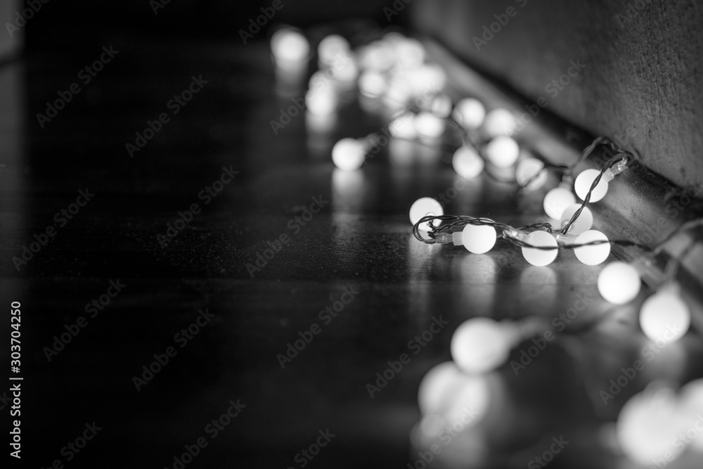 Black and white mood and tone of close up view of decorative wire led small warm white light bulbs lay on a floor at corner of dark and dim room. 