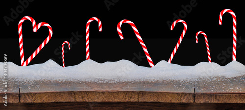 Sweet strieped candy canes in snow on wooden rustic table, isolated on black night background photo