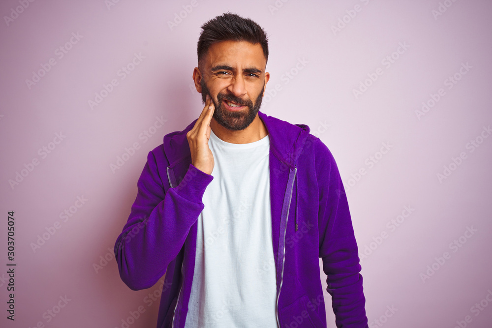 Fototapeta premium Young indian man wearing purple sweatshirt standing over isolated pink background touching mouth with hand with painful expression because of toothache or dental illness on teeth. Dentist concept.