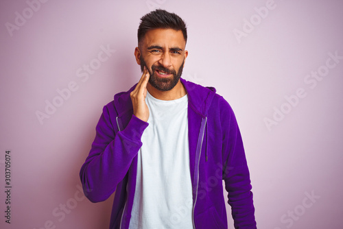 Young indian man wearing purple sweatshirt standing over isolated pink background touching mouth with hand with painful expression because of toothache or dental illness on teeth. Dentist concept. © Krakenimages.com