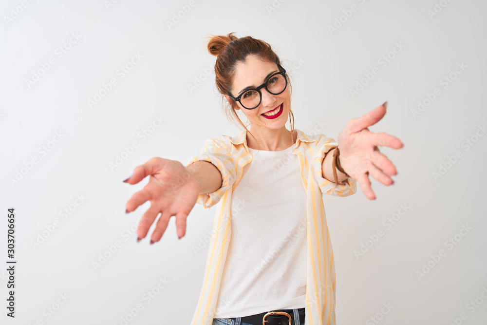 Redhead woman wearing striped shirt and glasses standing over isolated white background looking at the camera smiling with open arms for hug. Cheerful expression embracing happiness. - obrazy, fototapety, plakaty 