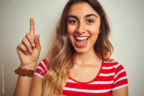 Young beautiful woman wearing red stripes t-shirt over white isolated background surprised with an idea or question pointing finger with happy face, number one