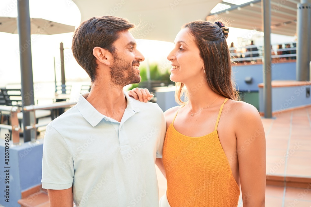 Young beautiful couple on vacation smiling happy and confident. Standing with smile on face hugging at the beach Young beautiful couple on vacation smiling happy and confident. Standing with smile on face hugging at the beach