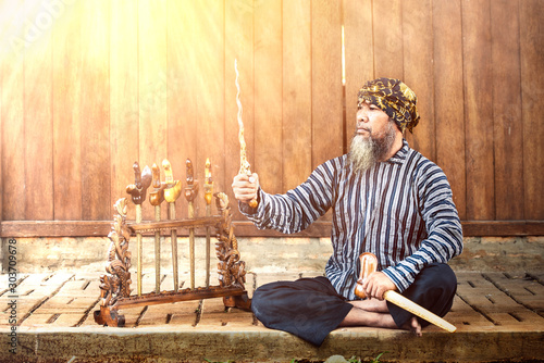 Asian old man showing his keris or kris collection with wooden wall background photo