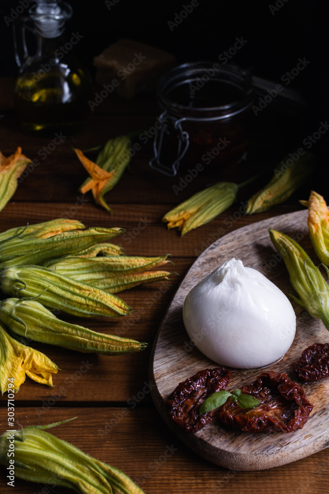 Φωτογραφία burrata cheese, dried tomatoes, zucchini flowers, olive oil on rustic wooden tab
