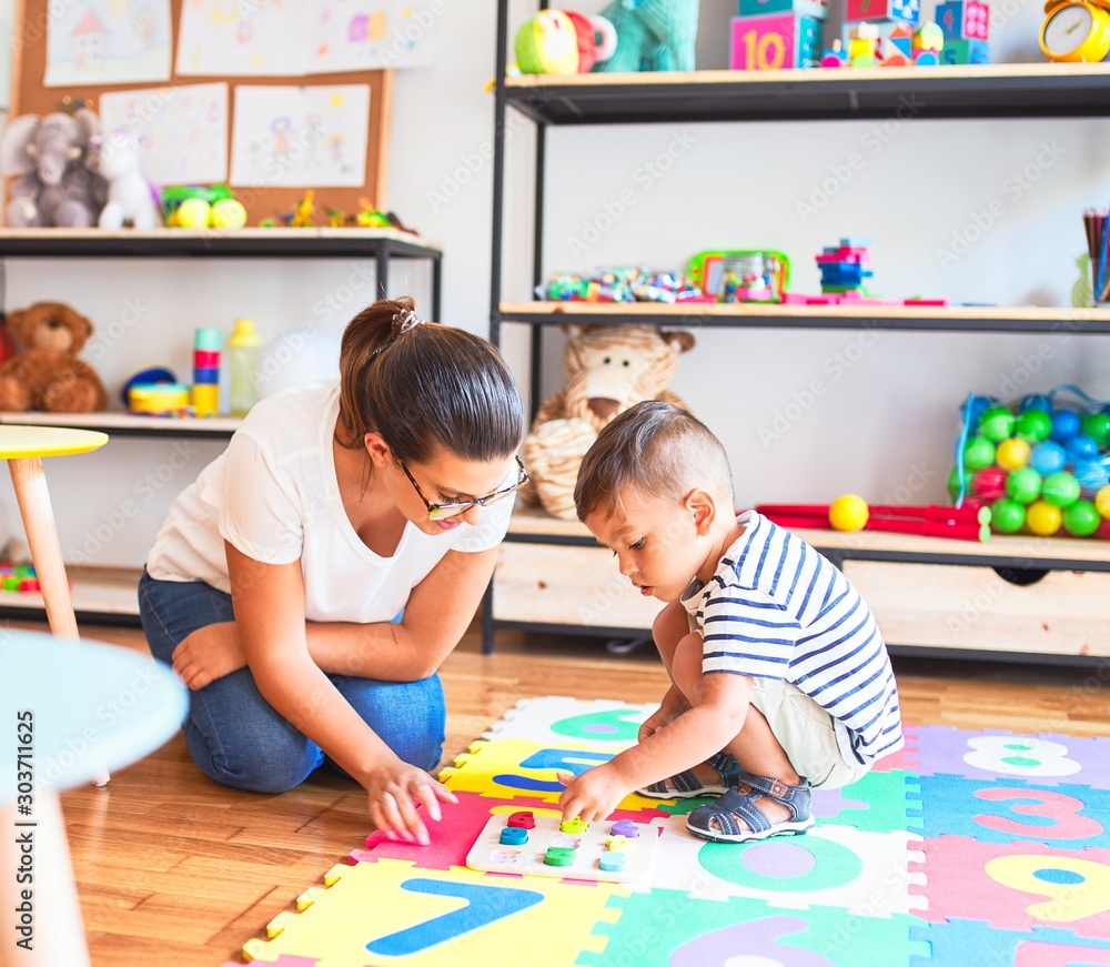 Fototapeta premium Beautiful teacher and toddler boy sitting on puzzle playing with numbers at kindergarten