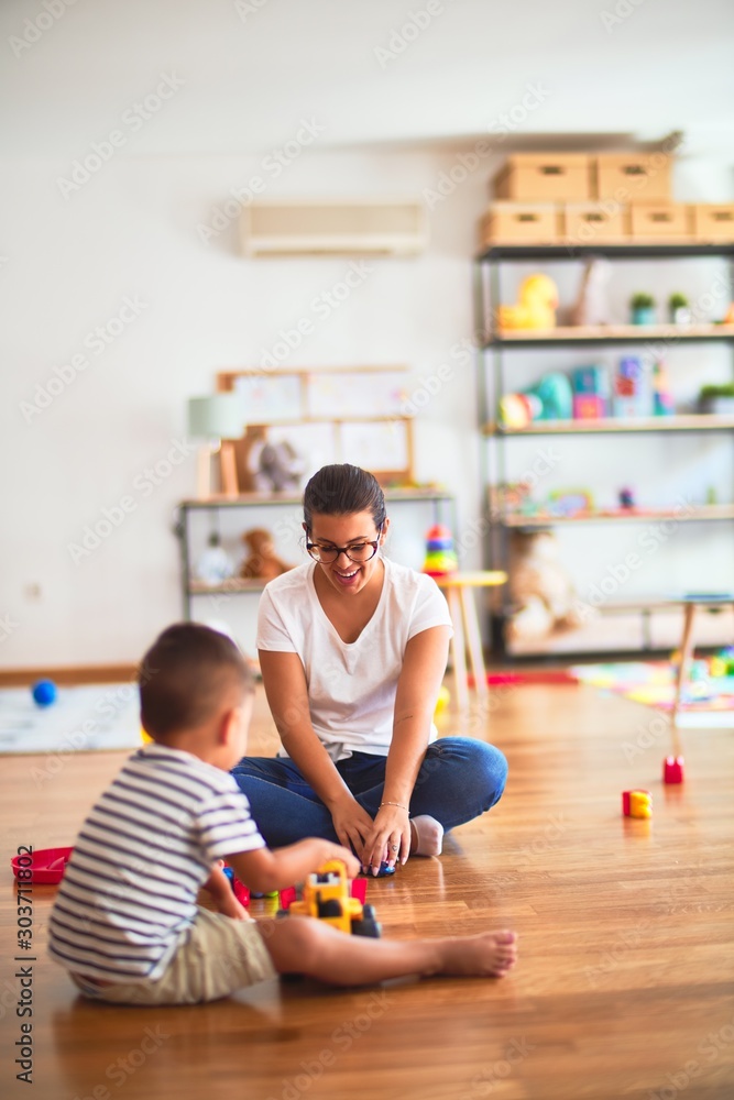 Fototapeta premium Beautiful teacher and toddler boy playing with tractor and cars at kindergarten