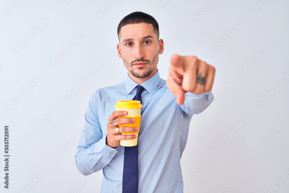 Young business man holding take away coffee over isolated background pointing with finger to the camera and to you, hand sign, positive and confident gesture from the front Young business man holding take away coffee over isolated background pointing with finger to the camera and to you, hand sign, positive and confident gesture from the front