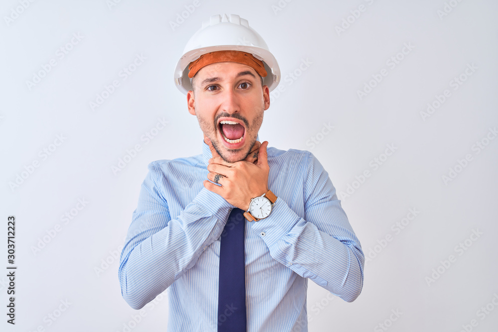 Young business man wearing contractor safety helmet over isolated background shouting and suffocate because painful strangle. Health problem. Asphyxiate and suicide concept. Young business man wearing contractor safety helmet over isolated background shouting and suffocate because painful strangle. Health problem. Asphyxiate and suicide concept.