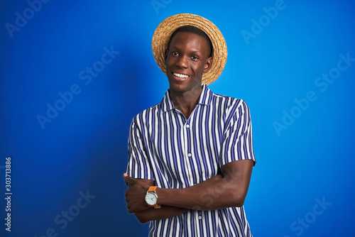 African american man wearing striped shirt and summer hat over isolated blue background happy face smiling with crossed arms looking at the camera. Positive person.