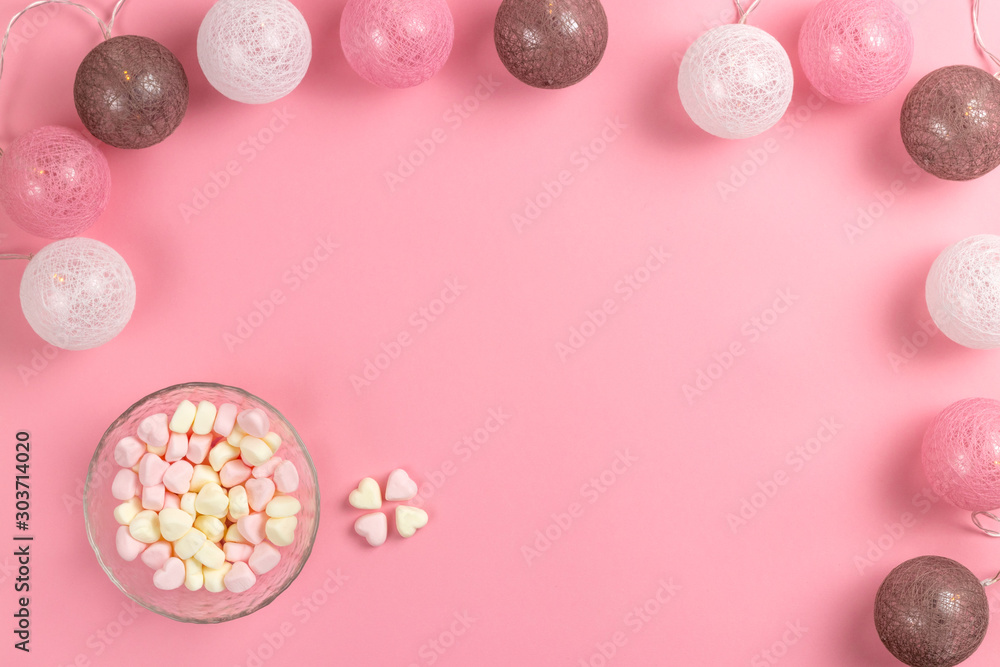 Composition for Valentine's Day February 14th. Delicate pink background and garland. Heart shaped yellow and pink marshmallows. Greeting card. Flat lay, top view, copy space.
