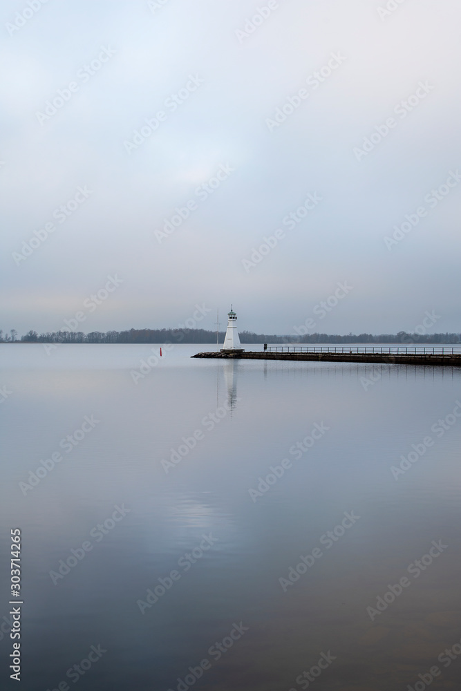 Lighthouse on pier reflecting in calm water.