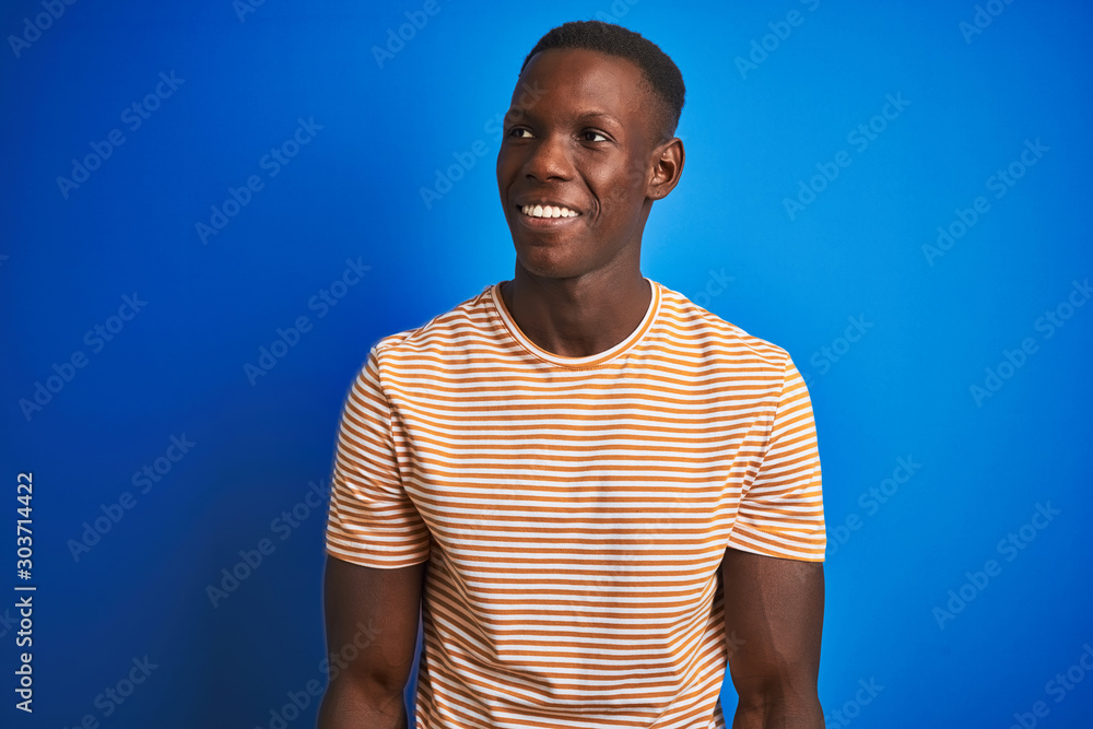 African american man wearing striped casual t-shirt standing over isolated blue background looking away to side with smile on face, natural expression. Laughing confident. African american man wearing striped casual t-shirt standing over isolated blue background looking away to side with smile on face, natural expression. Laughing confident.