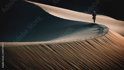 Woman walking along the ridge of a sand dune in the desert, Untied States photo