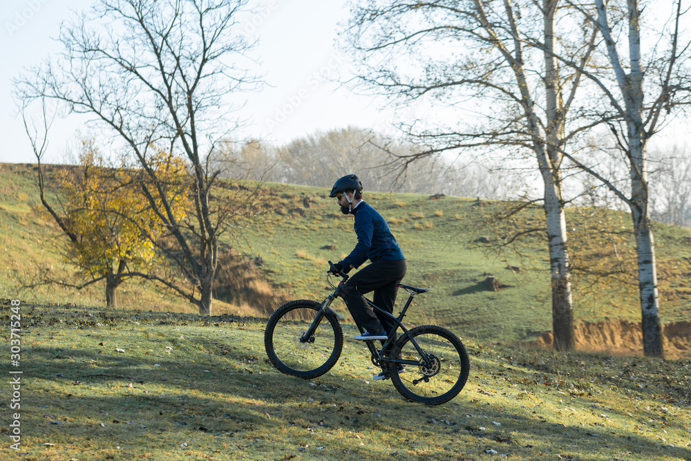 Cyclist in pants and fleece jacket on a modern carbon hardtail bike with an air suspension fork rides off-road.	