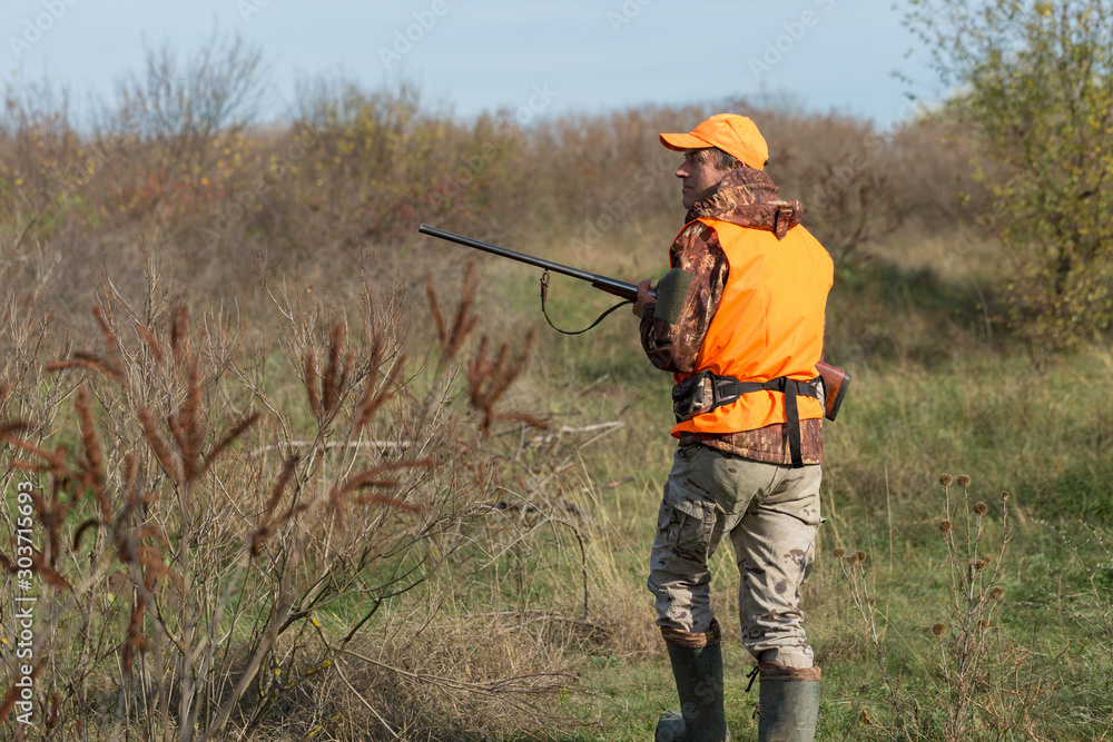 Hunting period, autumn season open. A hunter with a gun in his hands in hunting clothes in the autumn forest in search of a trophy. A man stands with weapons and hunting dogs tracking down the game. Hunting period, autumn season open. A hunter with a gun in his hands in hunting clothes in the autumn forest in search of a trophy. A man stands with weapons and hunting dogs tracking down the game.