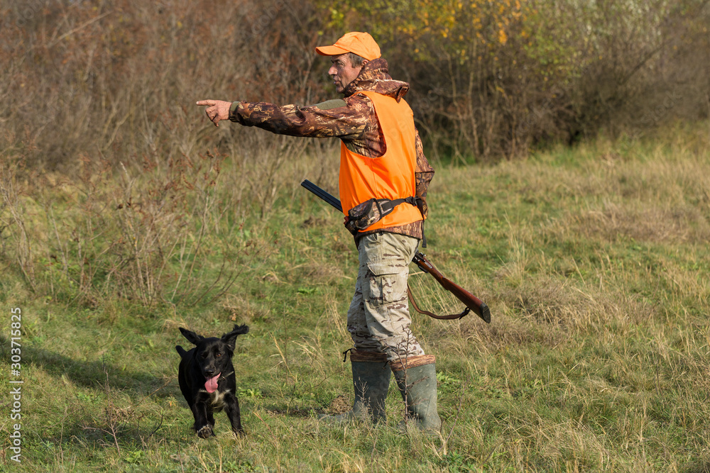 Hunting period, autumn season open. A hunter with a gun in his hands in hunting clothes in the autumn forest in search of a trophy. A man stands with weapons and hunting dogs tracking down the game. Hunting period, autumn season open. A hunter with a gun in his hands in hunting clothes in the autumn forest in search of a trophy. A man stands with weapons and hunting dogs tracking down the game.