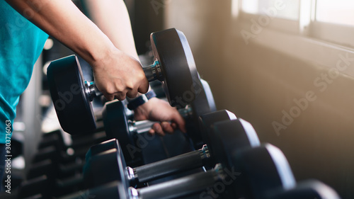 hands of man lifting dumbbells on rack in gym or fitness photo