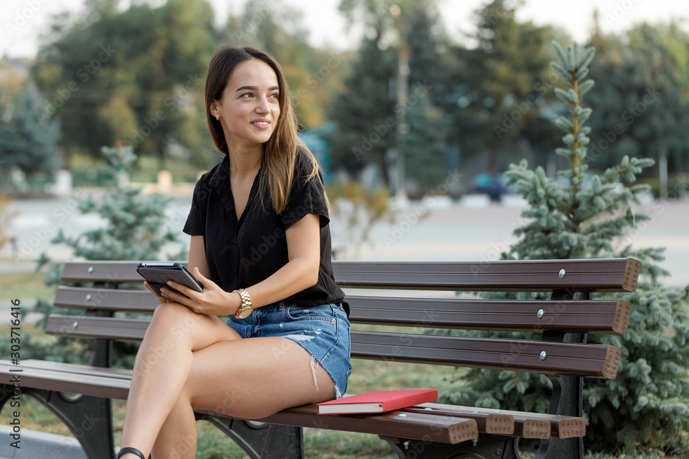 A young girl sits on a bench in a park and makes notes. Dressed in a free style. Business woman talking on the phone with customers. Time to relax and have some coffee A young girl sits on a bench in a park and makes notes. Dressed in a free style. Business woman talking on the phone with customers. Time to relax and have some coffee
