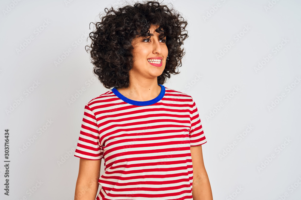Young arab woman with curly hair wearing striped t-shirt over isolated white background looking away to side with smile on face, natural expression. Laughing confident. Young arab woman with curly hair wearing striped t-shirt over isolated white background looking away to side with smile on face, natural expression. Laughing confident.