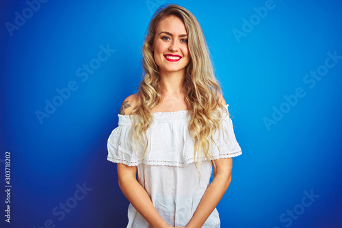 Young beautiful woman wearing white dress standing over blue isolated background with a happy and cool smile on face. Lucky person.