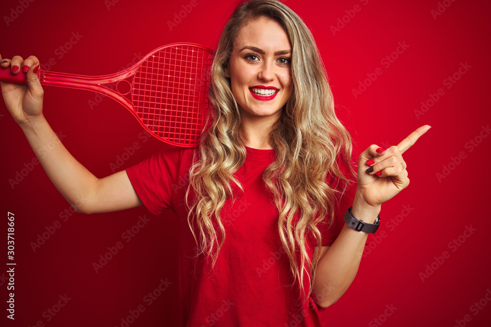 Young sportwoman playing tennis with racket and a ball over red isolated background very happy pointing with hand and finger to the side Young sportwoman playing tennis with racket and a ball over red isolated background very happy pointing with hand and finger to the side