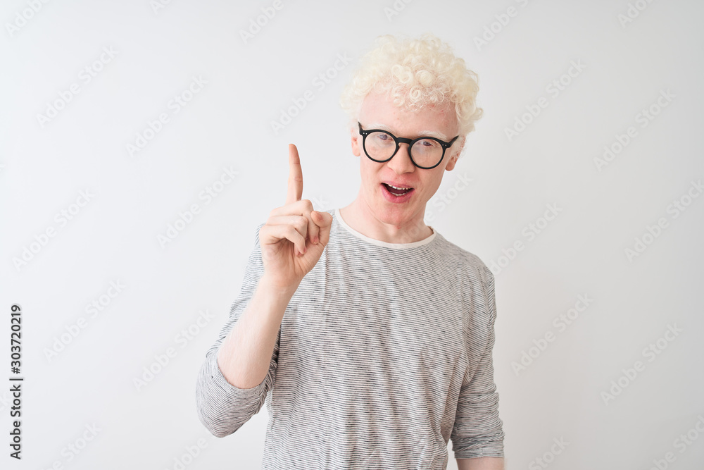 Young albino blond man wearing striped t-shirt and glasses over isolated white background pointing finger up with successful idea. Exited and happy. Number one. Young albino blond man wearing striped t-shirt and glasses over isolated white background pointing finger up with successful idea. Exited and happy. Number one.