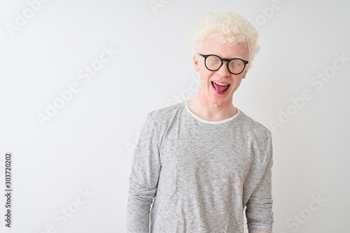 Young albino blond man wearing striped t-shirt and glasses over isolated white background sticking tongue out happy with funny expression. Emotion concept.