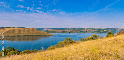 panorama landscape of nature reserve scenic view yellow grass land and hills around smooth lake reservoir in spring time clear weather day 