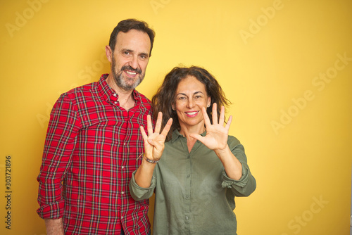 Beautiful middle age couple over isolated yellow background showing and pointing up with fingers number nine while smiling confident and happy.