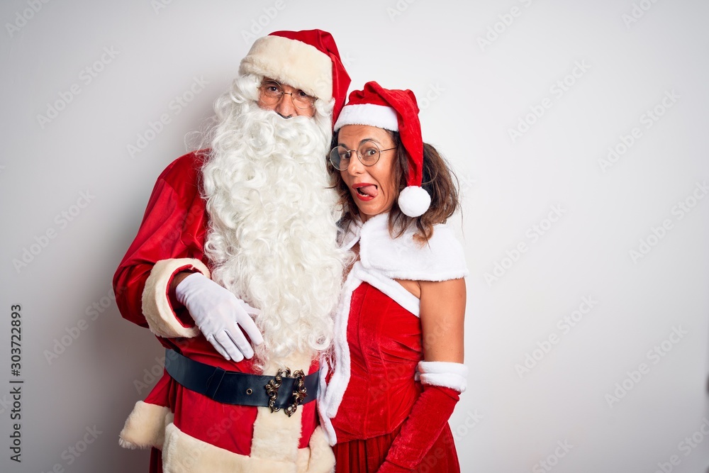 Middle age couple wearing Santa costume hugging over isolated white background sticking tongue out happy with funny expression. Emotion concept. Middle age couple wearing Santa costume hugging over isolated white background sticking tongue out happy with funny expression. Emotion concept.