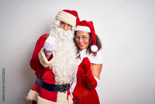 Middle age couple wearing Santa costume hugging over isolated white background doing money gesture with hands, asking for salary payment, millionaire business