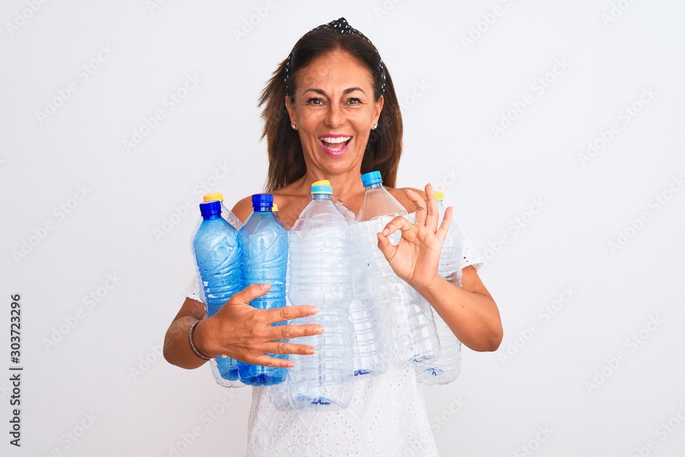 Middle age beautiful woman recycling plastic bottles standing over isolated white background doing ok sign with fingers, excellent symbol Middle age beautiful woman recycling plastic bottles standing over isolated white background doing ok sign with fingers, excellent symbol
