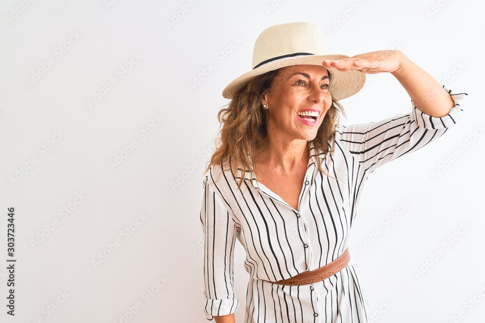 Middle age businesswoman wearing striped dress and hat over isolated white background very happy and smiling looking far away with hand over head. Searching concept. Middle age businesswoman wearing striped dress and hat over isolated white background very happy and smiling looking far away with hand over head. Searching concept.