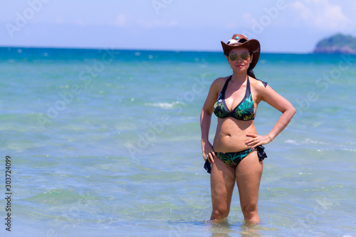 Woman with hat and bikini stand on beach