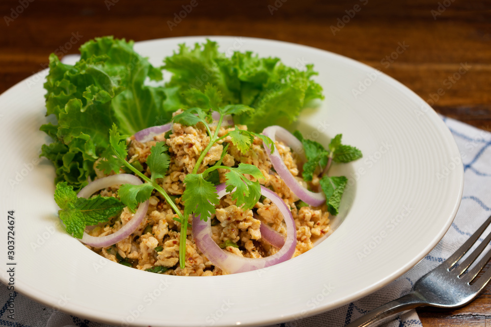 Spicy minced chicken with roasted rice and onion in white dish on wooden table.(Food of northeast in Thailand) Spicy minced chicken with roasted rice and onion in white dish on wooden table.(Food of northeast in Thailand)