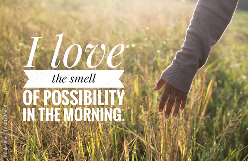 Inspirational motivational quote - I love the smell of possibility in the morning. With warm morning light over the field & young woman hand touch the leaves of paddy in field background. 