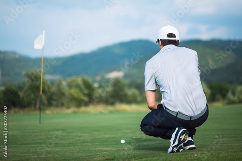 Pro golf player aiming shot with club on course. Male golfer on putting green about to take the shot..