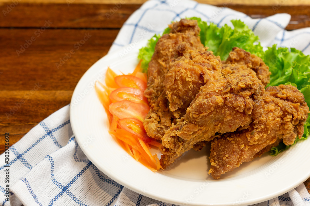 Fried chicken leg with tomato,carrot and lettuce in white dish on wooden table. Fried chicken leg with tomato,carrot and lettuce in white dish on wooden table.