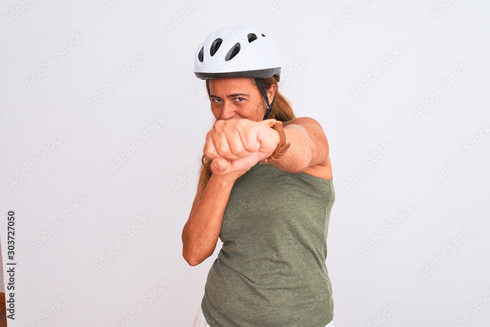 Middle age mature cyclist woman wearing safety helmet over isolated background Punching fist to fight, aggressive and angry attack, threat and violence Middle age mature cyclist woman wearing safety helmet over isolated background Punching fist to fight, aggressive and angry attack, threat and violence