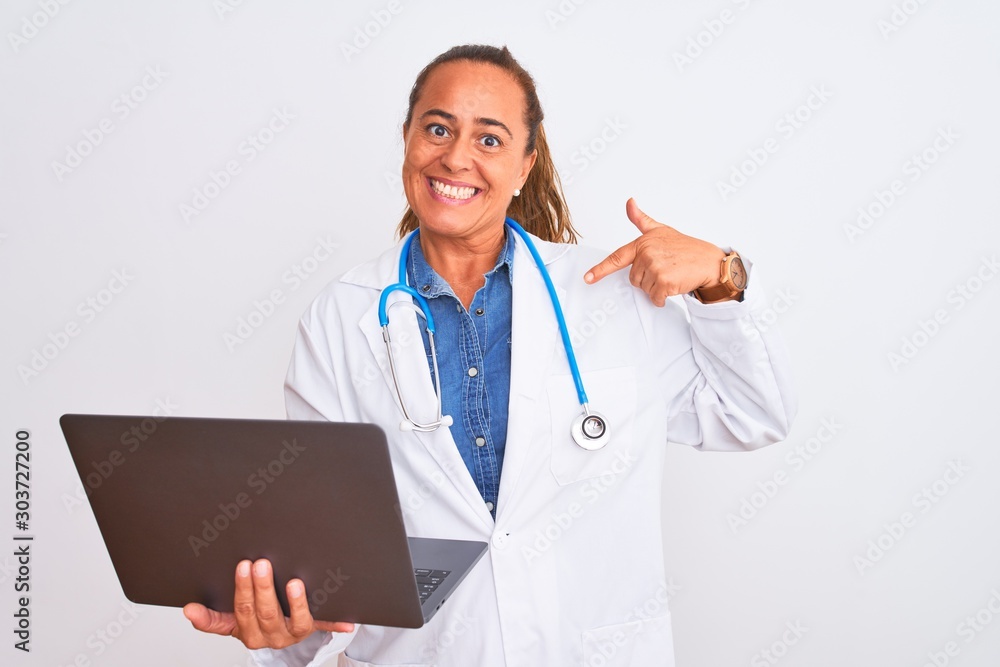 Middle age mature doctor woman holding computer laptop over isolated background with surprise face pointing finger to himself Middle age mature doctor woman holding computer laptop over isolated background with surprise face pointing finger to himself