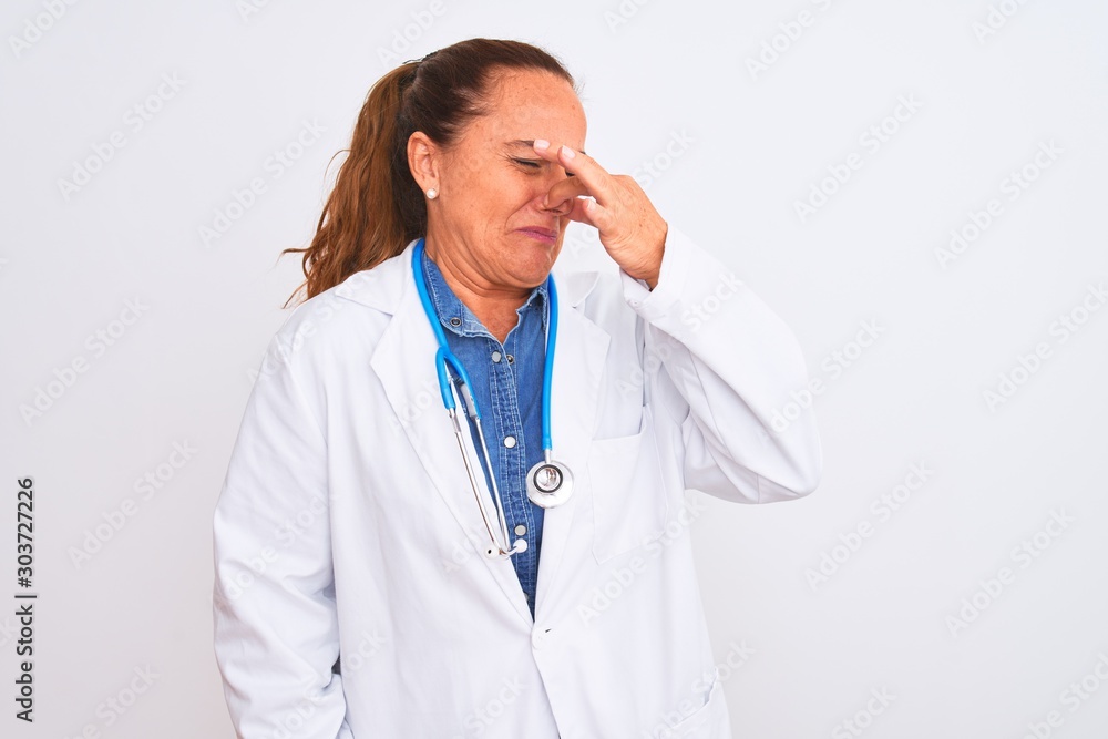 Middle age mature doctor woman wearing stethoscope over isolated background smelling something stinky and disgusting, intolerable smell, holding breath with fingers on nose. Bad smells concept. Middle age mature doctor woman wearing stethoscope over isolated background smelling something stinky and disgusting, intolerable smell, holding breath with fingers on nose. Bad smells concept.