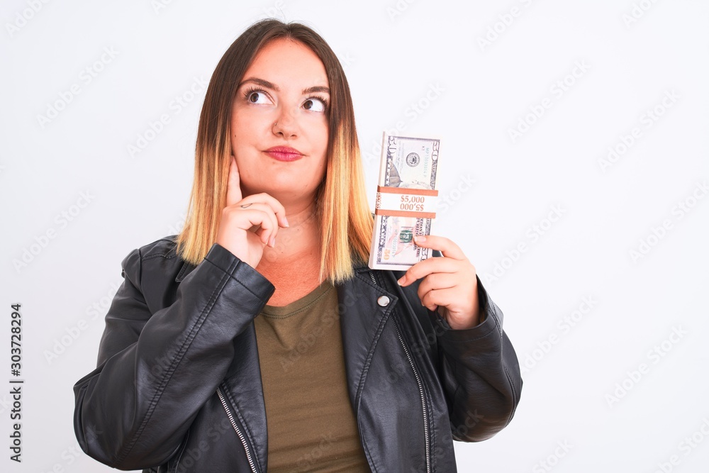 Young beautiful woman holding dollars standing over isolated white background serious face thinking about question, very confused idea Young beautiful woman holding dollars standing over isolated white background serious face thinking about question, very confused idea