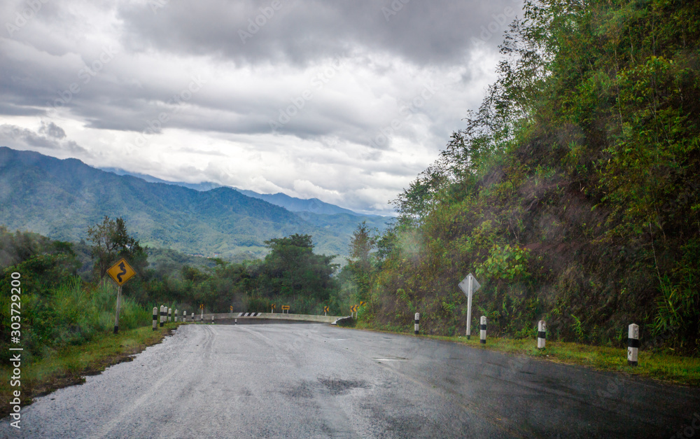 Blurred background of a mountain road view, from a car windscreen that runs with care, with natural scenery surrounded by plants, large trees
