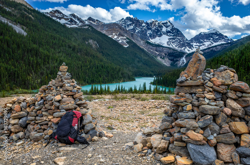 View ro the beautiful canadian landscape with tarquin lake and snowy mountains in the background, and red backpack and stone wall in foreground, vivid colours  photo