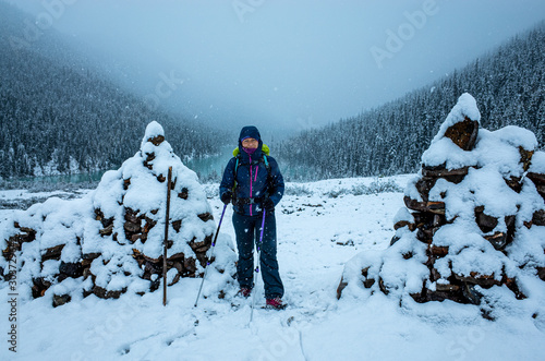 Young adventure healthy woman is hiking in the winter, Fryatt valley trail in Jasper National park,  Alberta, Canada. Solo woman in the summer snow storm is smiling to the camera  photo