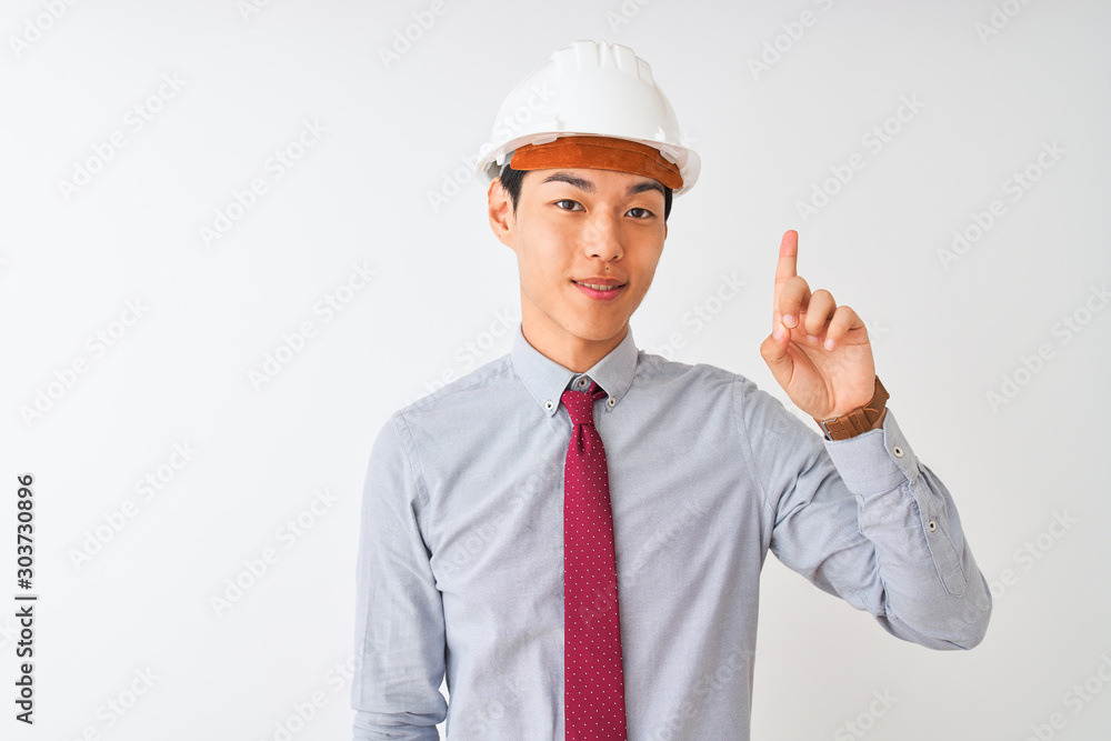 Chinese architect man wearing tie and helmet standing over isolated white background showing and pointing up with finger number one while smiling confident and happy.